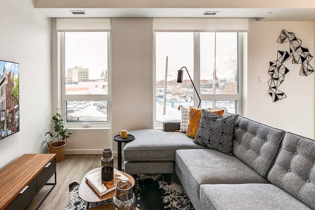 A grey couch sits in a living room with a large window showing a snowy landscape outside.