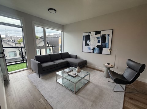 A modern living room with a grey sofa, a glass coffee table, and a black chair.