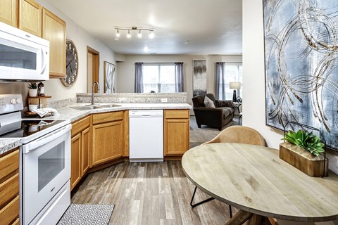 A kitchen with a white oven and microwave, wooden cabinets, a round table, and a large abstract painting on the wall.