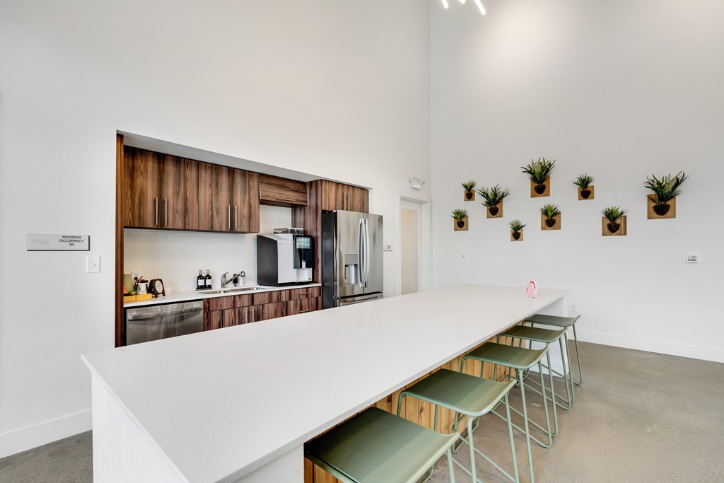 A white table with green chairs is in front of a wall with a picture of a kitchen.