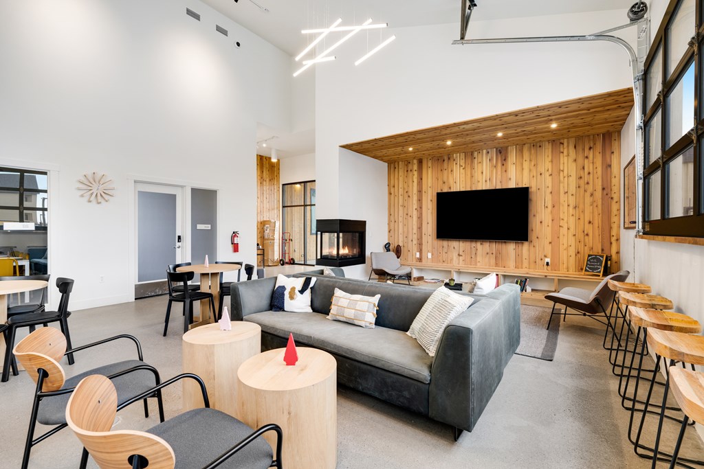 A modern living room with a grey couch, wooden chairs, and a flat screen TV.