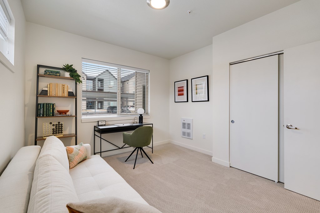 A room with a white sofa, a desk with a chair, and a bookshelf with various items.