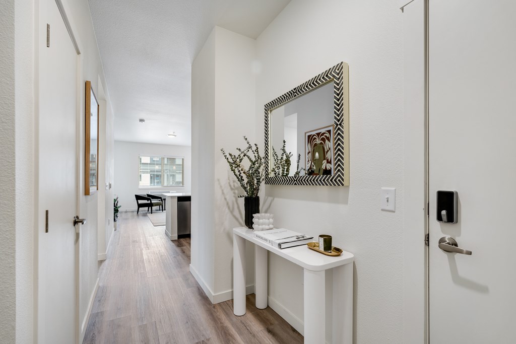 A hallway with a mirror and a table with a vase of flowers on it.