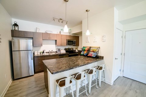 A kitchen with a refrigerator, stove, and bar stools.