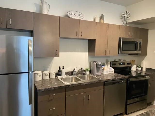 A kitchen with a refrigerator, microwave, oven, and sink.