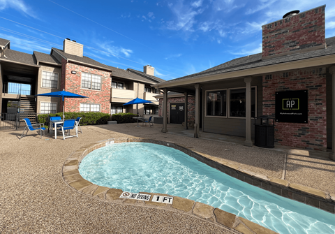 A pool surrounded by a brick building and chairs.
