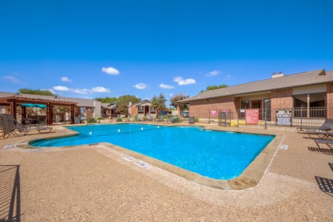 A large outdoor swimming pool surrounded by a sandy area and a few chairs.