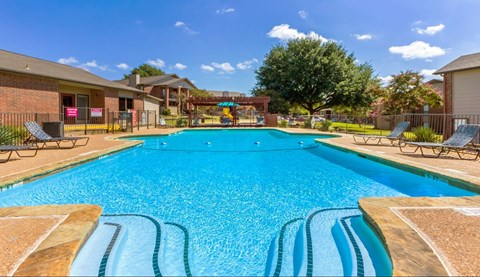 A large blue swimming pool with a wooden deck and lounge chairs.