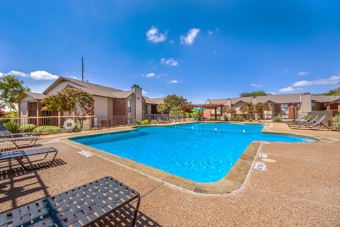 A large outdoor swimming pool surrounded by sun loungers and a building in the background.