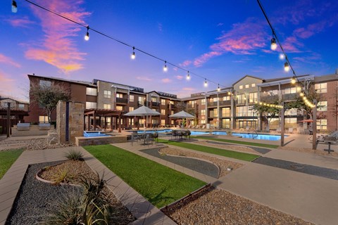 Outdoor courtyard with pool lawn and string lights at dusk at Gateway Cedars Apartments, Forney, TX