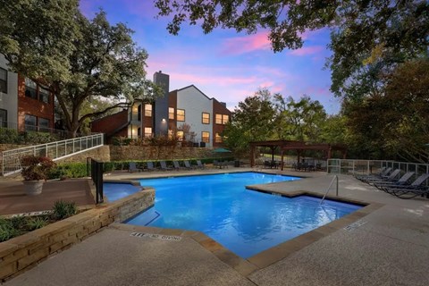 A swimming pool surrounded by a stone wall with a building in the background.