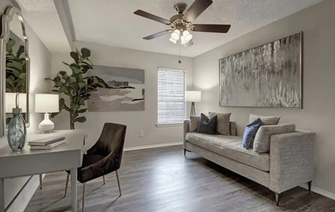 A living room with a grey couch, a chair, a table with a vase and a lamp on it, and a painting on the wall.