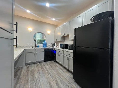 A black refrigerator sits in a kitchen with white cabinets and a wooden floor.