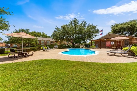 A pool surrounded by a grassy area and a picnic table.