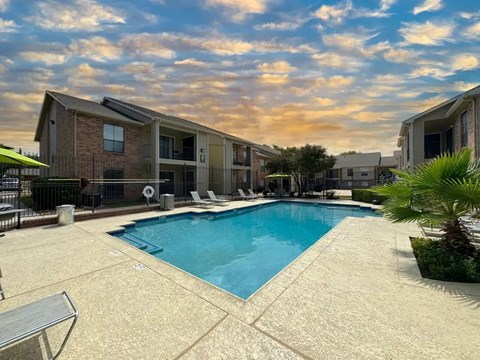 Resort style pool with lounge chairs and umbrellas at Village Green Apartments, San Marcos, TX