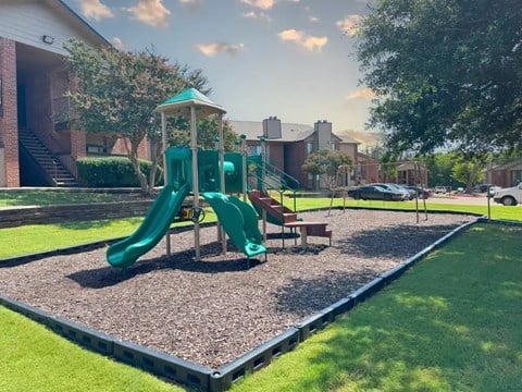 A playground with a green slide and a wooden bench.