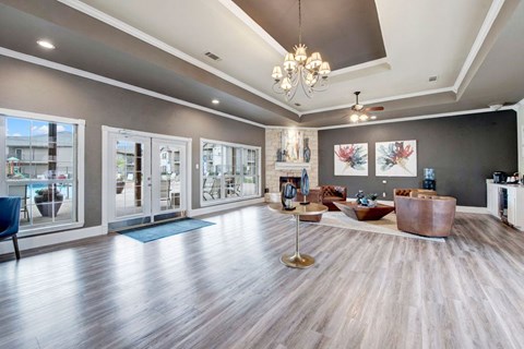 A spacious living room with a large window, a wooden floor, and a chandelier.