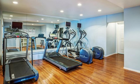 a gym with cardio equipment and mirrors in a room with wood floors