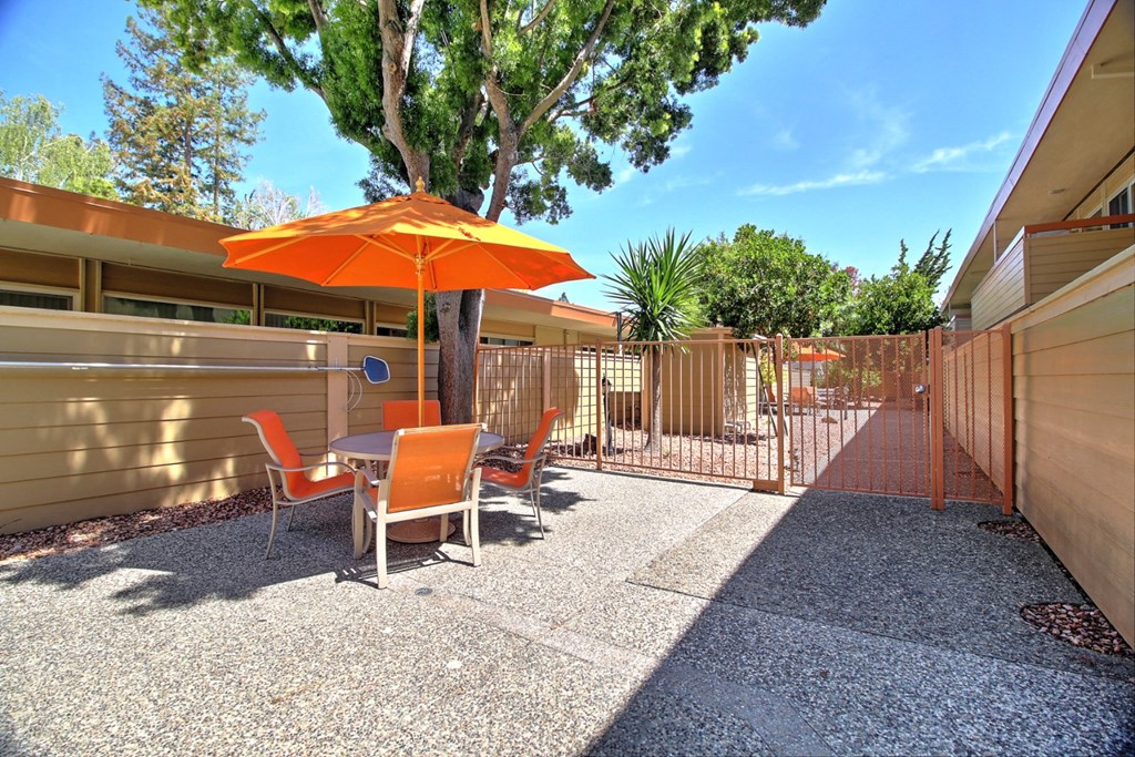 a patio with an orange umbrella and chairs and a fence
