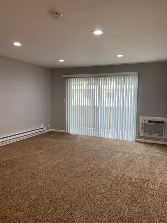 A room with a carpeted floor and a window with blinds.
