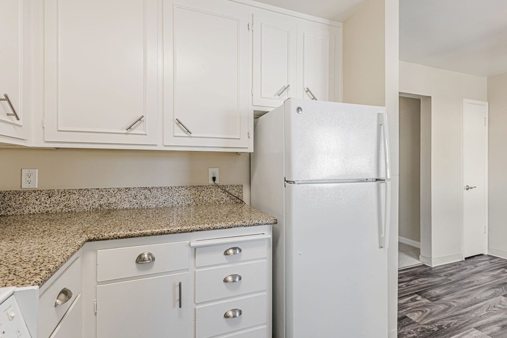 A white refrigerator in a kitchen with white cabinets.