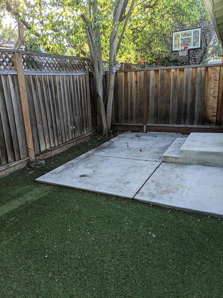 A backyard with a basketball hoop and a wooden fence.