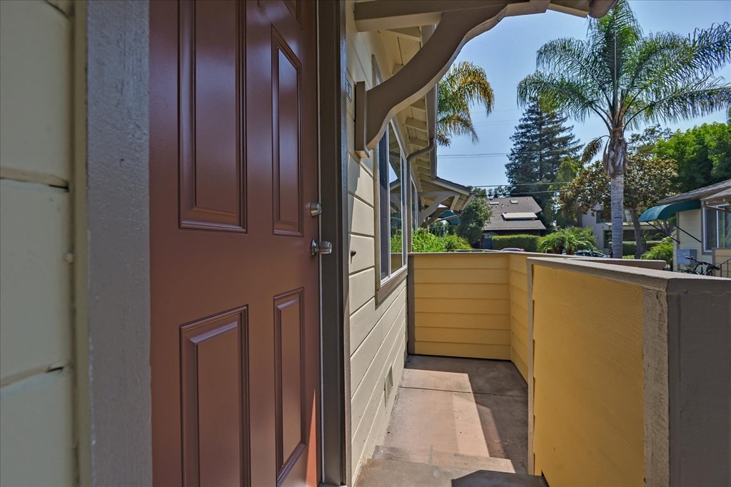 A brown door is open to a patio with a view of a house and trees.