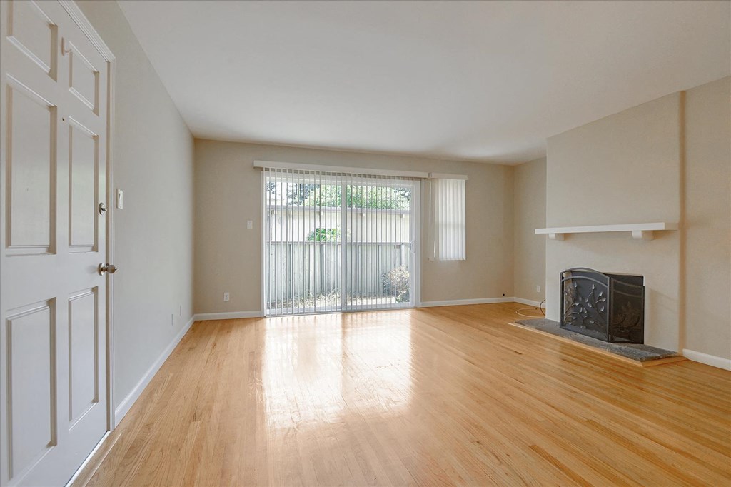 an empty living room with a fireplace and wood floors