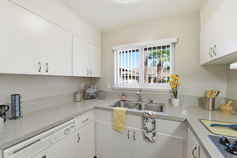 A kitchen with white cabinets and a window with a view of a balcony with a yellow towel hanging on the sink.