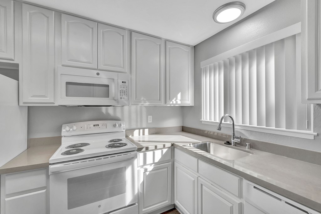 A white kitchen with a stove, microwave, and sink.