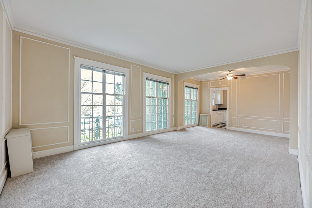 A large, empty room with a carpeted floor and a window with a view of a balcony.