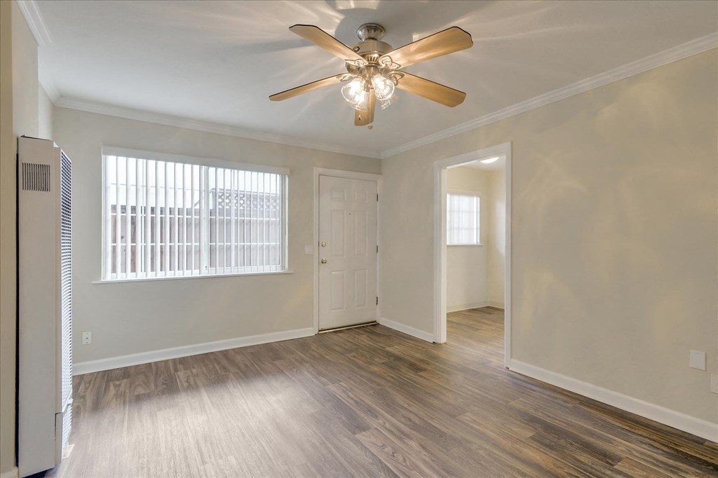an empty living room with a ceiling fan and a door to a bedroom