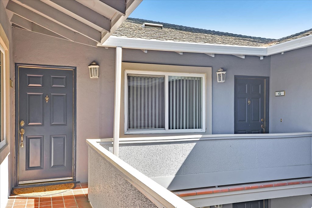 A grey house with a black door and a window with white curtains.