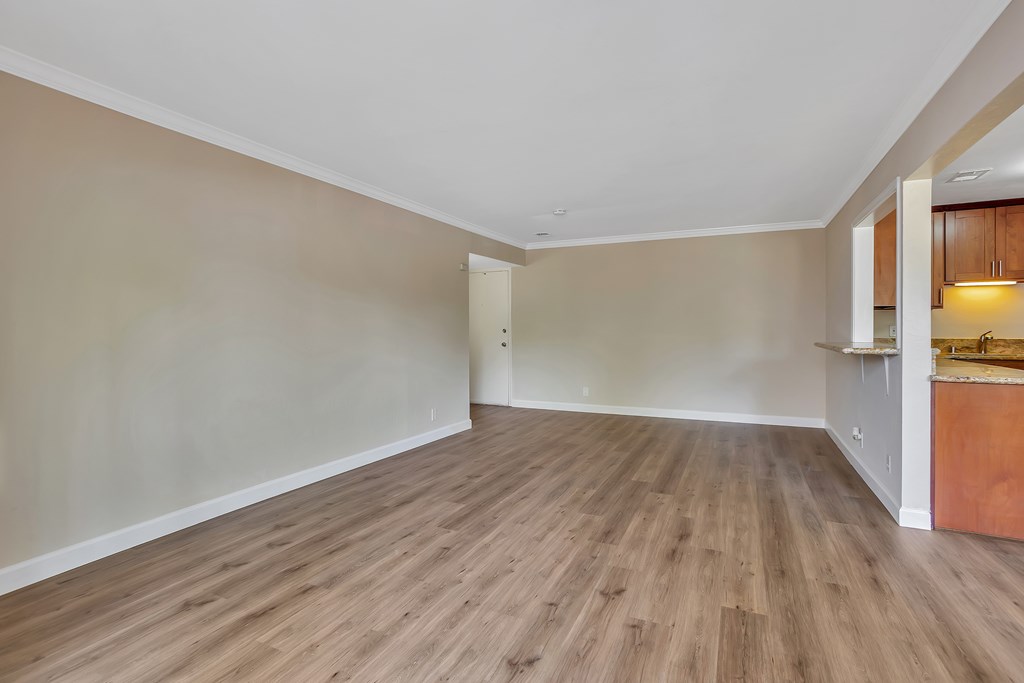 A room with wooden flooring and a kitchen area in the background.