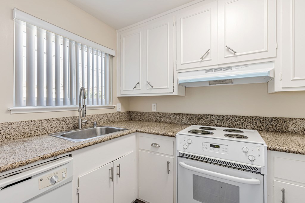 A white stove and sink in a kitchen with white cabinets.