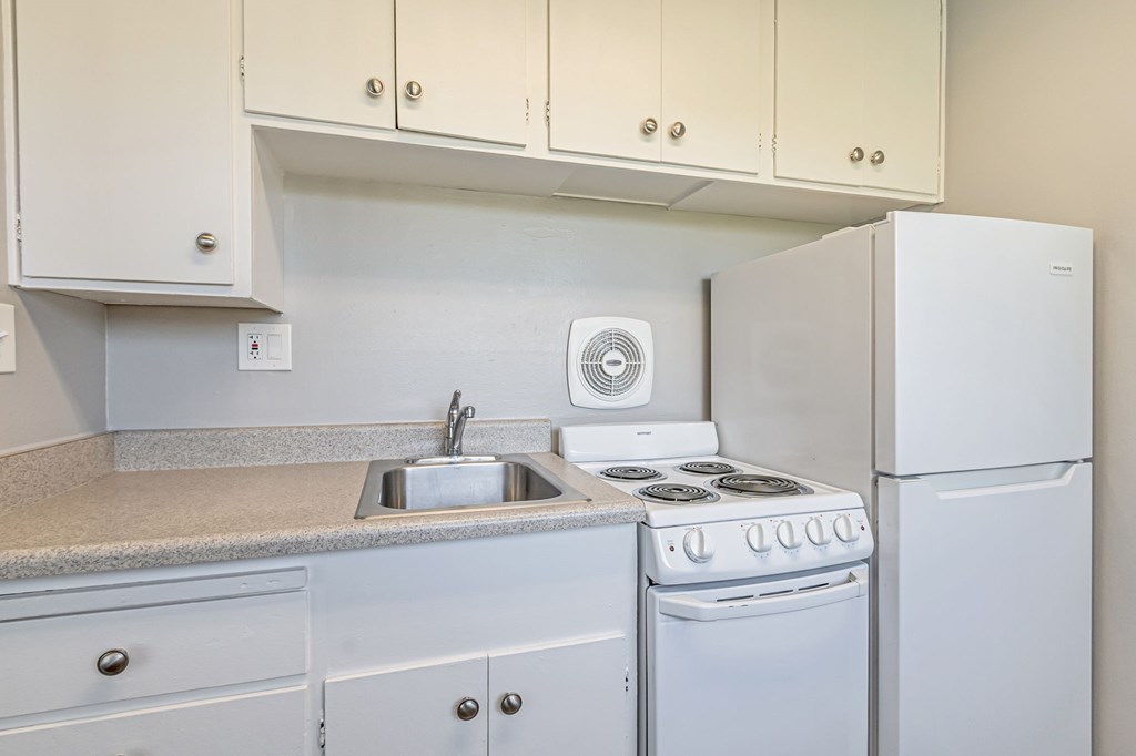 A white kitchen with a stove, sink, and cabinets.
