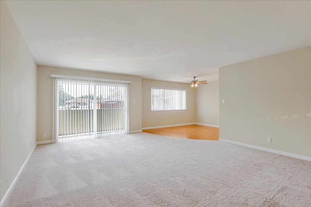 an empty living room with a large window and a ceiling fan