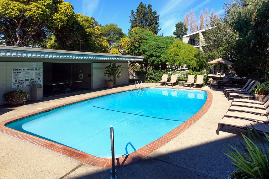 a large swimming pool with lounge chairs and trees in the background