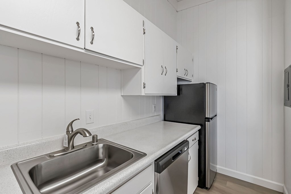 A kitchen with a black fridge and a stainless steel sink.