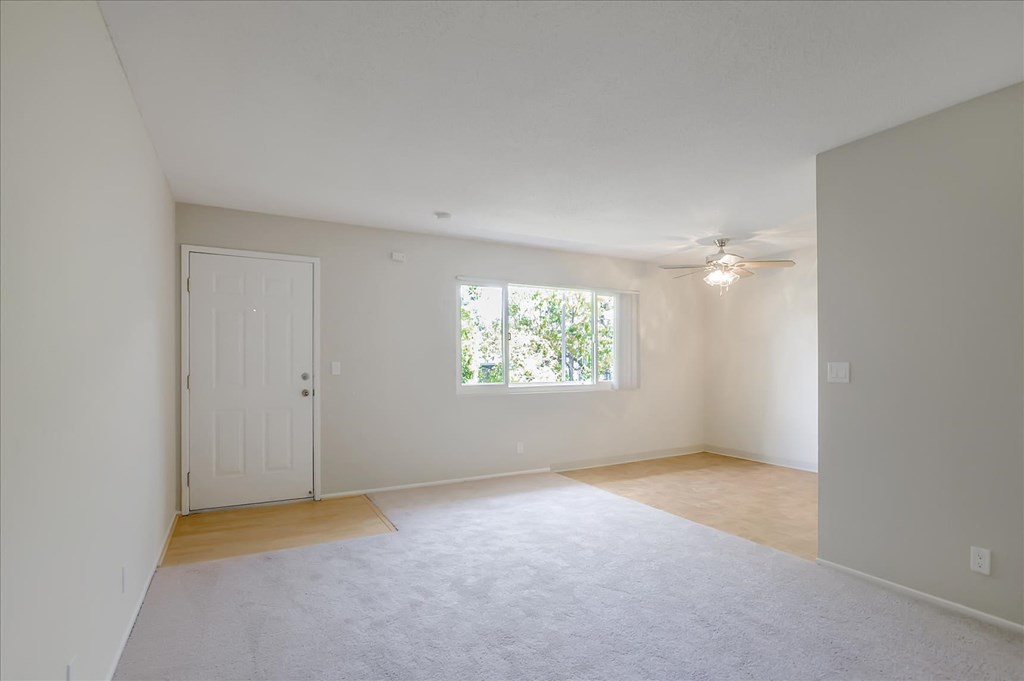 an empty living room with a ceiling fan and a window
