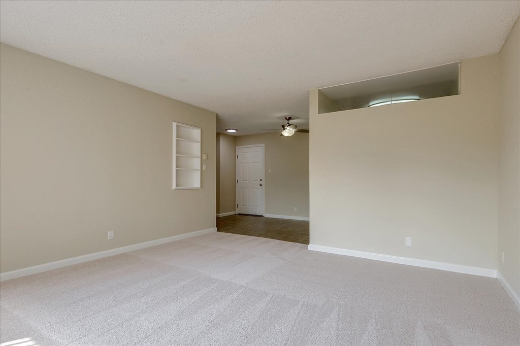 an empty living room with white carpet and a door to a closet