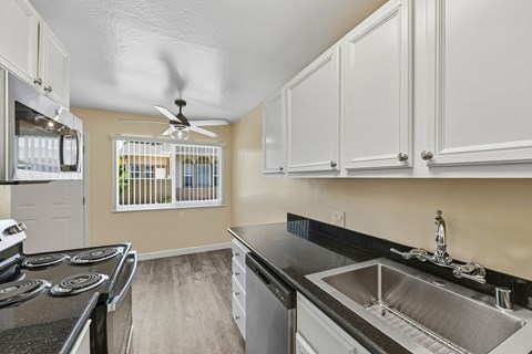 A kitchen with a stove top oven, sink, and cabinets.