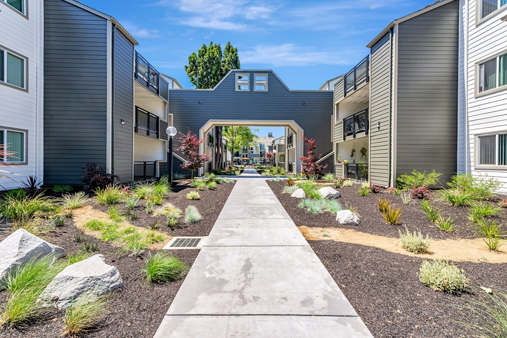 A concrete pathway leads through a landscaped courtyard between two buildings.