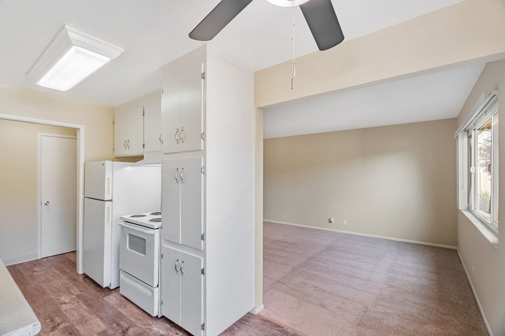 A kitchen with white appliances and a ceiling fan.