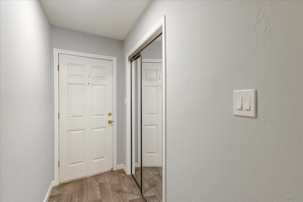 A white door with a gold handle is in a room with a light switch on the wall.