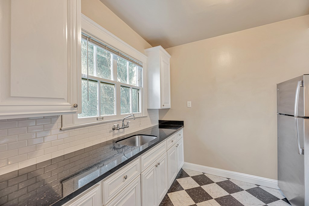 A kitchen with white cabinets and a black and white checkered floor.