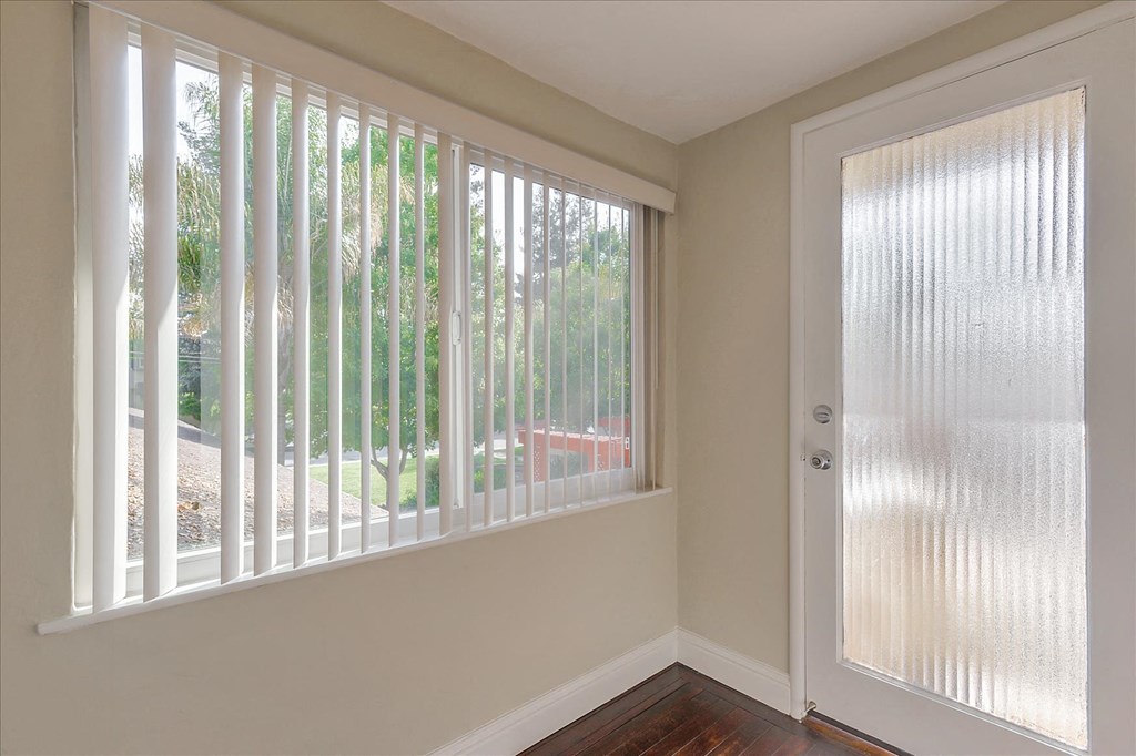a living room with a large window and a door with vertical blinds