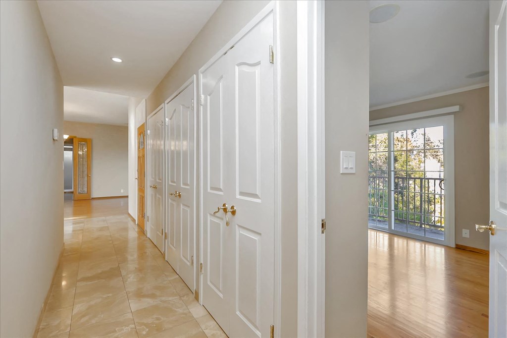 a long hallway with white doors and a door to a balcony