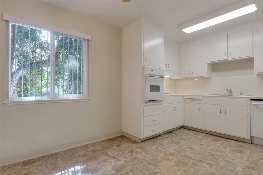 A kitchen with white cabinets and a window with trees outside.
