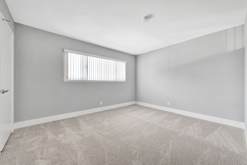A room with a carpeted floor and a window with blinds.